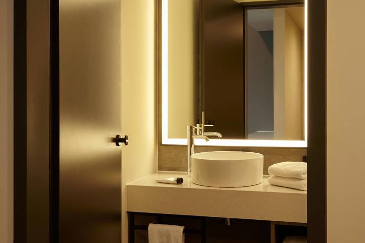 Waschtisch im modernen Design mit zahlreichen Handtüchern sowie großem, beleuchtetem Spiegel in der Replay Suite King.