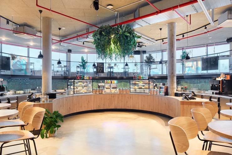 Theke des Cafés mit großer Auswahl an Snacks und Süßem. Darum herum moderne Holz-Sitzgruppen.