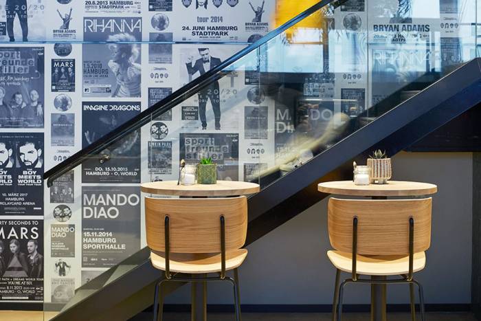 Café und Bar mit Wanddekoration aus schwarz-weißen Musik-Plakaten, davor moderne Stühle aus Holz.