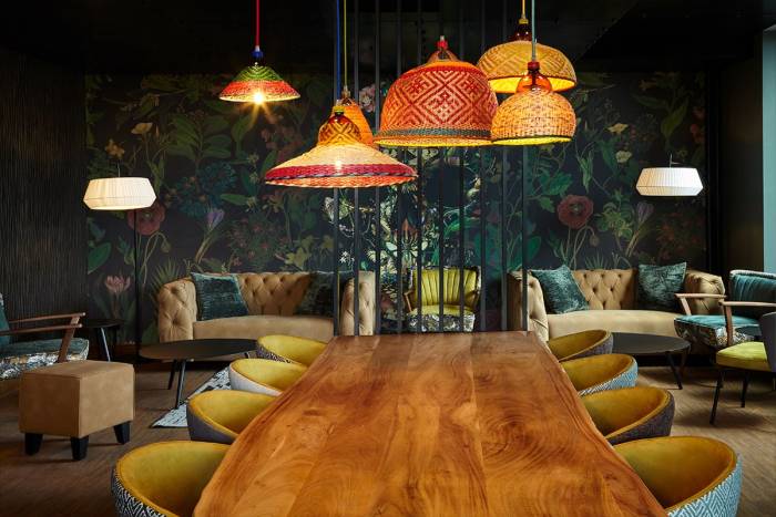 Ess- und Loungebereich, mit Holztisch, Polstermöbeln und großzügigen Naturelementen in tiefen Grün- und Gelbtönen.