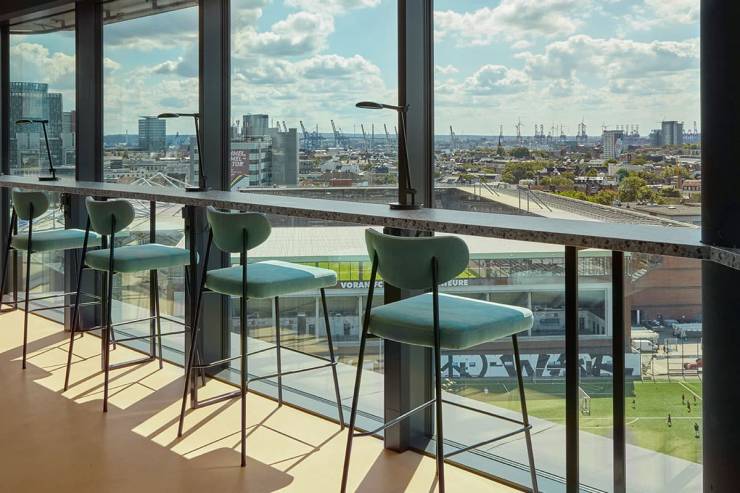 Hellblau gepolsterte Barstühle an der Fensterfront zum Millerntor-Stadion. Hafenkräne am Horizont.