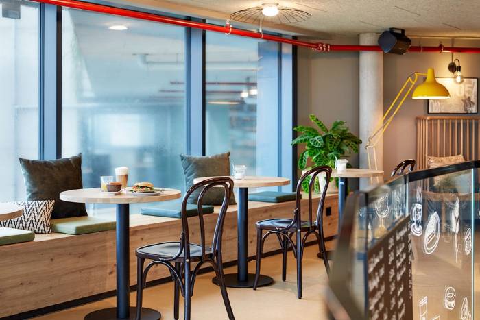 Schlichte, moderne Holzsitzbank mit Kissen, kombiniert mit Retro-Café-Stühlen und -Lampen.