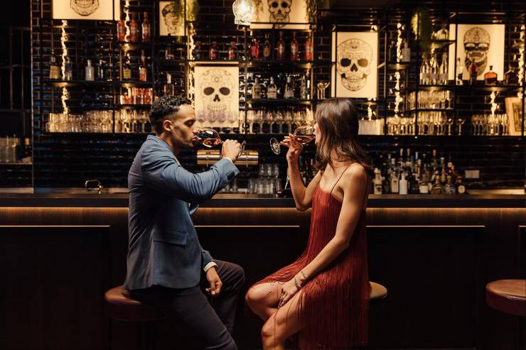 Bar im Retro-Look mit Barhockern, ein Paar trinkt gemeinsam Wein.