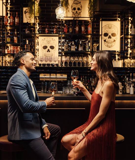 Zwei Personen sitzen an der Bar im KARO&PAUL, mit leckeren Drinks in der Hand, und lächeln sich gegenseitig an.