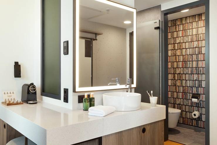 Bad im REVERB Hotel Hamburg mit großem Waschtisch, beleuchteten Spiegeln und RITUALS-Produkten für eine Portion Wellness.