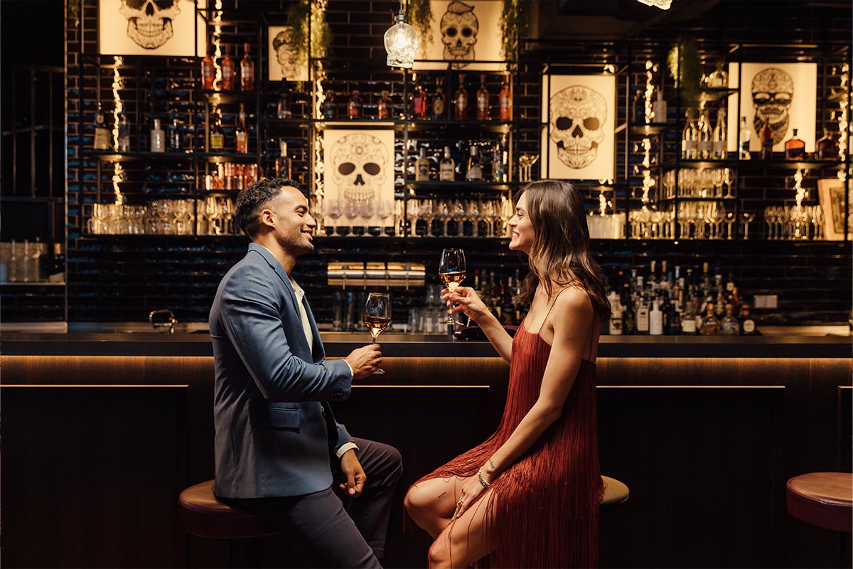 Zwei Personen sitzen an der Bar im KARO&PAUL, mit leckeren Drinks in der Hand, und lächeln sich gegenseitig an.