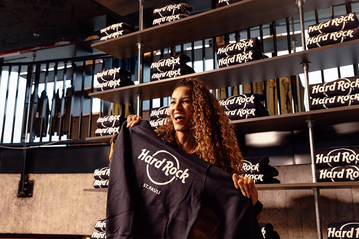 Eine Frau hält ein Hard Rock St. Pauli T-Shirt in der Hand. Im Hintergrund sind weitere T-Shirts.